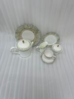 A 24-piece luxury porcelain tea set featuring white ceramic with a soft green brushstroke border and gold-tone accents, arranged on a light wooden table.