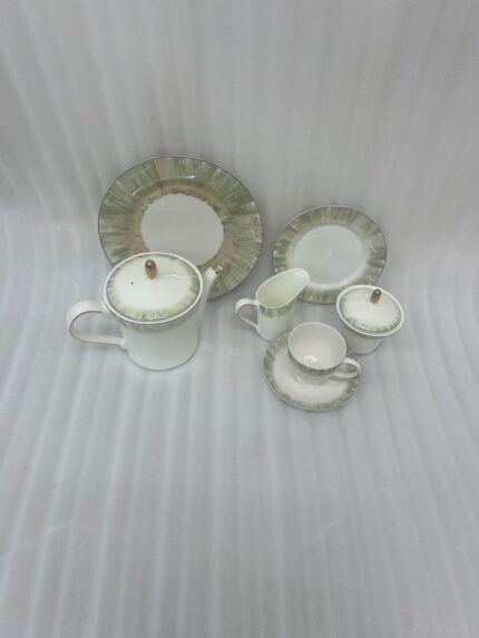 A 24-piece luxury porcelain tea set featuring white ceramic with a soft green brushstroke border and gold-tone accents, arranged on a light wooden table.