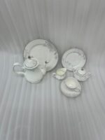 A 24-piece white porcelain tea set featuring delicate gray floral patterns and silver trim, arranged on a light wooden surface.