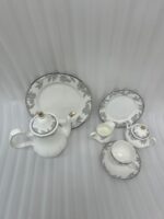 A 24-piece luxury porcelain tea set featuring a white teapot, milk jug, sugar pot, cups, saucers, and plates adorned with delicate gray floral patterns and gold rims on a wooden table.