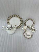 : A complete 24-piece porcelain tea and dining set featuring white ceramic with gold and olive-green striped rims, including plates, cups, saucers, a teapot, a sugar bowl, and a milk creamer arranged on a wooden surface.