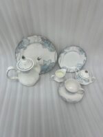 A 24-piece luxury porcelain tea set featuring a delicate blue floral pattern and silver trim, including a teapot, cups, saucers, plates, sugar bowl, and milk jug on a linen runner.