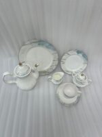 A luxurious 24-piece porcelain tea set featuring white ceramic with blue marble patterns and gold trim, displayed on a marble surface.