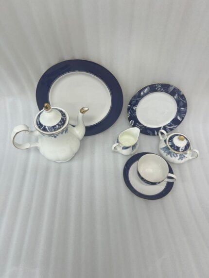 A 24-piece luxury porcelain tea set featuring a classic blue and white floral pattern with gold trim, including a teapot, cups, saucers, and plates, arranged on a beige table runner.