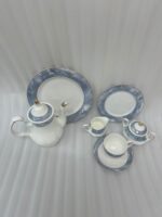 A 24-piece luxury porcelain tea set featuring a white base with elegant blue marble-patterned rims and gold accents, displayed on a textured stone surface including a teapot, cups, saucers, plates, sugar pot, and creamer.