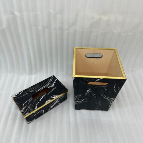 A matching executive desk accessory set featuring a black marble pattern wastebasket and a rectangular tissue box cover with elegant gold trim, placed on a dark wooden office desk.