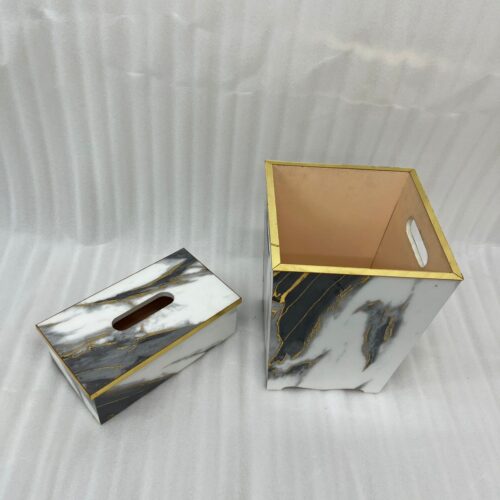 A luxury white and black marble-patterned tissue box holder and matching wastebasket with elegant gold trim, displayed on a wooden table.