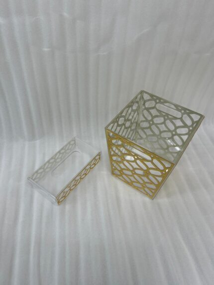 Clear acrylic dustbin and matching tissue box holder with a gold geometric lattice pattern on a white marble tabletop.