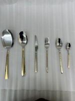 High-end 36-piece stainless steel cutlery set featuring polished silver heads and gold handles with a geometric Greek key pattern, arranged elegantly on a dark wooden table.