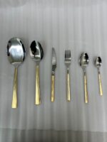 A 36-piece luxury One More cutlery set featuring elegant gold-accented handles with a geometric Greek key pattern, arranged professionally on a dark wood dining table.