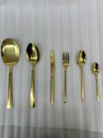 Luxury 36-piece gold-finished cutlery set featuring a geometric Greek key handle design, displayed elegantly on a dark grey placemat.