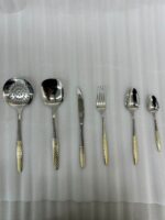 A complete 36-piece stainless steel cutlery set arranged on a dark wooden dining table, showcasing elegant gold-textured handles, including knives, forks, various spoons, and serving utensils.