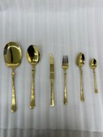 High-angle studio shot of a 36-piece gold-plated cutlery set arranged on a polished wooden surface, featuring matching serving pieces, dinner spoons, forks, knives, and teaspoons with elegant handle detailing.