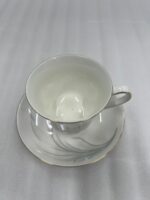Steaming hot tea in an elegant white bone china teacup with gold trim and a silver leaf design, resting on a matching saucer on a wooden table