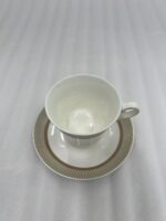 A premium white Super Bone China tea cup and saucer set featuring gold vertical stripes and a gold laurel wreath pattern on a dark wooden table