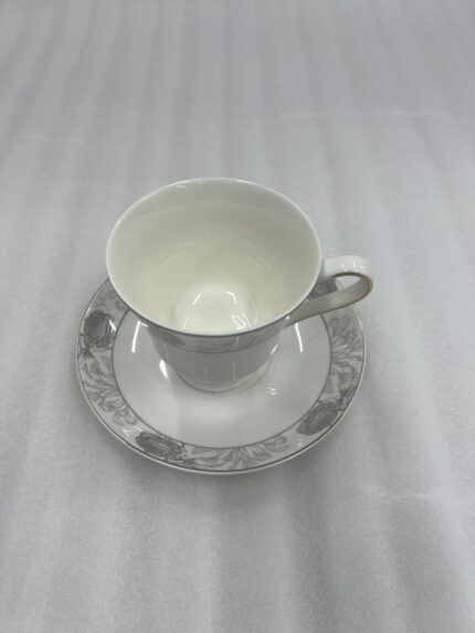 Elegant white Super Bone China teacup and saucer featuring a grey floral pattern and gold rim, placed on a wooden table next to a silver spoon and lavender vase