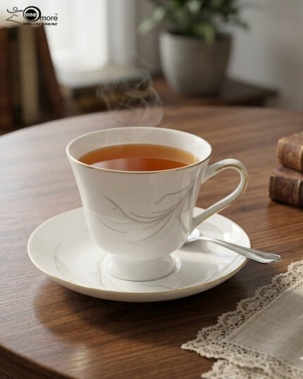 Steaming hot tea in an elegant white bone china teacup with gold trim and a silver leaf design, resting on a matching saucer on a wooden table