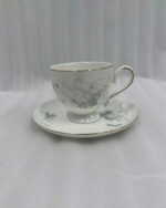 A steaming cup of black tea in a white bone china cup featuring blue floral patterns and a gold rim, resting on a matching saucer on a dark wooden table