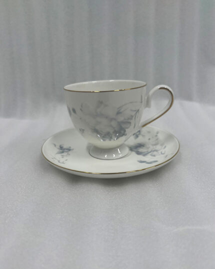 A steaming cup of black tea in a white bone china cup featuring blue floral patterns and a gold rim, resting on a matching saucer on a dark wooden table