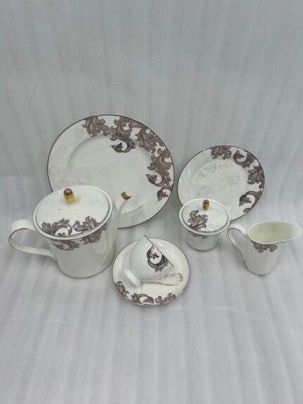 An elegant white and grey floral tea set on a wooden table, featuring a person pouring milk into a cup of tea alongside a plate of toasted rusks.