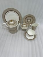 A premium Super Bone China tea set featuring a teapot, sugar bowl, creamer, and cups and saucers with a tan pinstripe pattern and gold-rimmed borders, arranged on a wooden table outdoors with avocado toast on a plate.