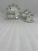 A luxury super bone china teacup and saucer set featuring a grey floral rose pattern, shown on a formal wooden dining table with a matching teapot and breakfast setting.