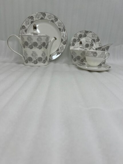 A luxury super bone china teacup and saucer set featuring a grey floral rose pattern, shown on a formal wooden dining table with a matching teapot and breakfast setting.