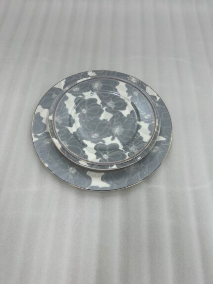 A stacked 18-piece super bone china dinnerware set featuring a grey and white floral pattern on a wooden table, including rice, deep, and quarter plates.