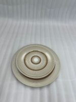 A stacked 18-piece super bone china plate set with a gold sunburst design on a wooden dining table.