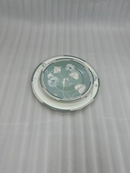 A stack of 18 super bone china plates featuring a sage green and white floral design, including rice plates, deep plates, and quarter plates, displayed on a white damask runner