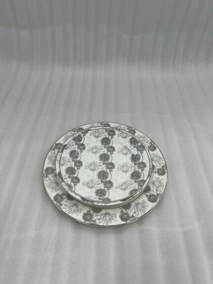 Stacked 18-piece super bone china plate set with grey floral patterns, including rice plates, deep plates, and quarter plates on a wooden dining table.