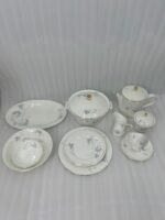 High-angle view of a 61-piece white super bone china dinner set with blue floral patterns and gold rims, elegantly arranged for an 8-person serving on a long mahogany dining table with blue chairs.