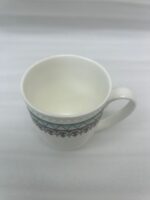A premium bone china mug filled with hot tea on a black marble countertop, featuring a turquoise geometric pattern and silver lace design, set against a cozy kitchen background with soft natural lighting