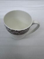 A steaming cup of green tea in a white bone china mug with a bronze geometric pattern and embossed lattice texture, sitting on a wooden table