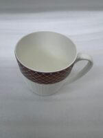 A luxury white bone china mug with a rose gold mesh design on the rim, filled with steaming green tea and a tea leaf floating on top, placed on a textured placemat with a silver spoon on a wooden dining table