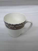 A high-angle shot of a white bone china mug filled with tea, featuring a gold geometric pattern on a wooden outdoor table with a gold spoon and green garden background