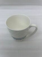A set of white bone china mugs featuring a diamond-embossed top half and a decorative gold and teal traditional pattern at the bottom, filled with steaming tea on a wooden desk