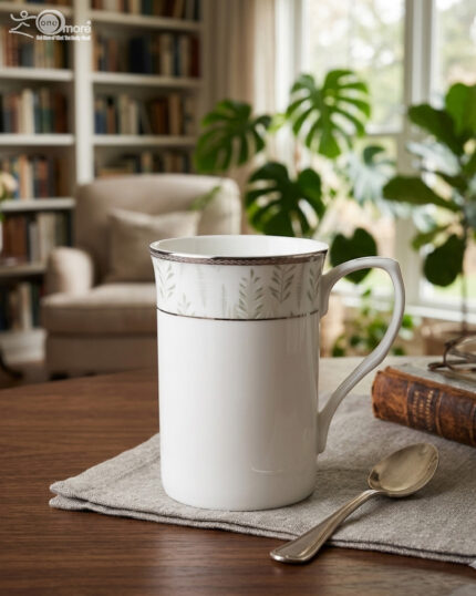 A professional lifestyle shot (3.jpg) showcasing two white Bone China mugs with silver rims and a green botanical leaf pattern, featuring one tall "long" mug and one "short" mug on a linen cloth in a cozy living room setting