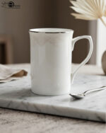 A set of two white bone china mugs on a wooden surface, one short and one tall, featuring elegant gold lace patterns and metallic gold rims against a neutral background.