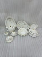 Luxury Super Bone China dinnerware set featuring a delicate white floral pattern, gold-rimmed edges, and matching tea service pieces on a wooden surface
