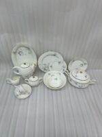 A complete super bone china dinner set in file 3.jpg featuring a delicate blue rose pattern, gold-rimmed edges, and including a teapot, plates, bowls, and serving dishes on a marble surface.