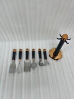A 7-piece kitchen gadget set featuring black matte handles and rose gold accents, displayed on a matching rotating stand atop a white marble kitchen counter.