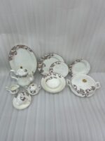 An elegant white super bone china dinner set featuring a classic brown and gold baroque acanthus leaf pattern, including plates, bowls, a teapot, a tureen, and teacups arranged on a light-colored surface