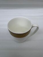 A set of elegant white bone china mugs with an embossed diamond pattern and a golden basket-weave rim, filled with steaming hot tea on a wooden table.