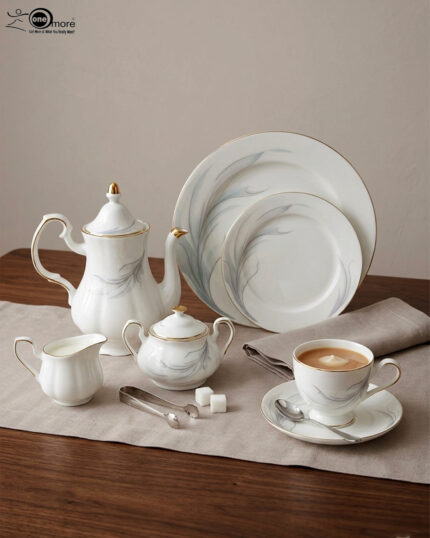 An elegant white super bone china dinner set with gold rims and a delicate grey leaf pattern, displayed on a wooden table
