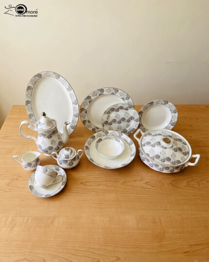 An elegant white and grey floral patterned super bone china dinner set arranged on a wooden table, including plates, bowls, a teapot, a casserole dish, and teacups.