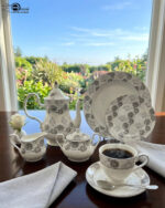 An elegant white and grey floral patterned super bone china dinner set arranged on a wooden table, including plates, bowls, a teapot, a casserole dish, and teacups.