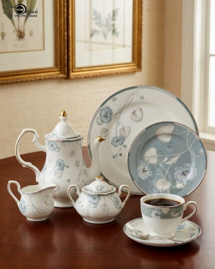 A premium super bone china tea set featuring a classic teapot, sugar bowl, creamer, teacup with saucer, and matching plates, all adorned with an elegant light blue and grey floral pattern on a wooden table.