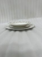 A stacked 18-piece premium super bone china dinnerware set with elegant floral and striped rim borders, neatly arranged on a dark wooden dining table next to a crystal glass and fabric napkin