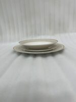 A neatly stacked 18-piece super bone china dinner plate set with elegant gold borders, arranged on a beige placemat next to a gold fork, a gold knife, and a crystal wine glass on a wooden table.